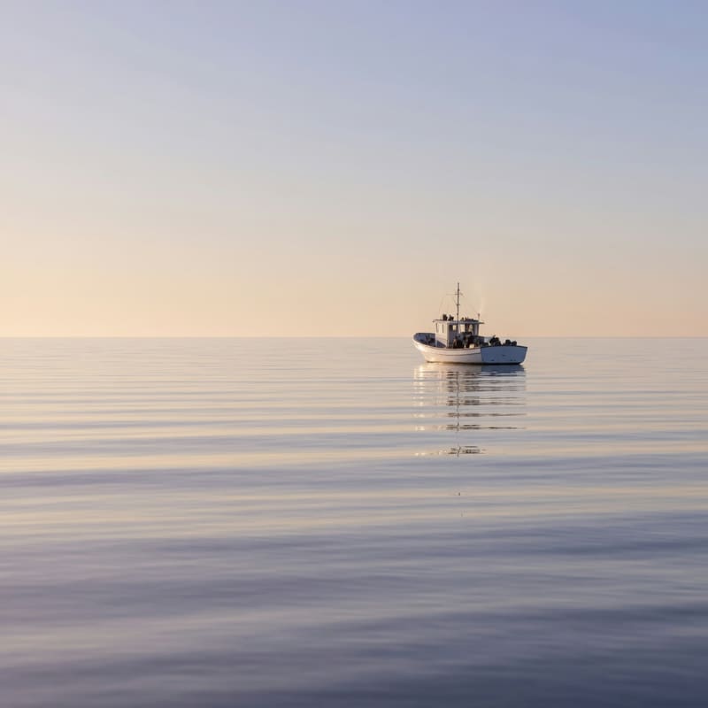 A calm, glassy sea at dawn with a small fishing boat far off